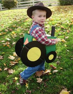 a young boy wearing a tractor costume in the grass with leaves on the ground around him