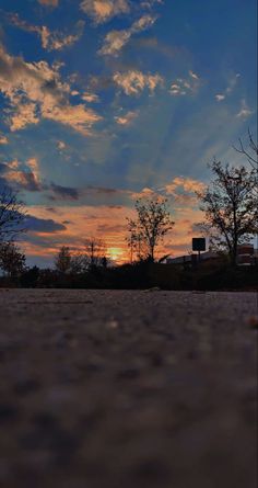 the sun is setting behind some clouds in the sky over a parking lot with trees