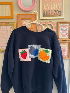 a blue sweatshirt with fruit on it is hanging in front of a wall full of framed pictures