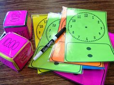 a pile of colorful dices sitting on top of a wooden table next to a clock