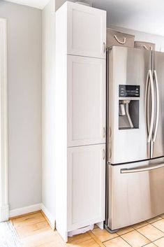 a stainless steel refrigerator and freezer combo in a kitchen with white walls, tile flooring and wooden floors