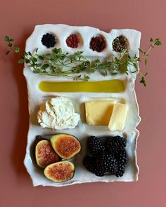 an assortment of cheeses and fruits on a tray with herbs, berries, and butter