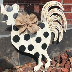 a wooden rooster with a bow on it's head sitting in front of a brick wall