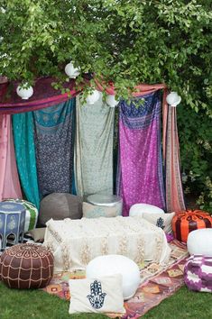 an image of a bed and pillows on the ground in front of some trees with colorful curtains