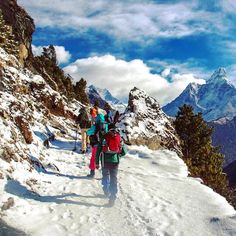 several people hiking up a snowy mountain with mountains in the background