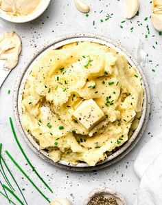 a bowl filled with mashed potatoes topped with butter and seasoning next to garlic