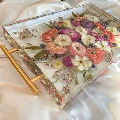 a glass box filled with flowers on top of a white table cloth covered bedding