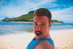 a man making a funny face on the beach with an island in the back ground