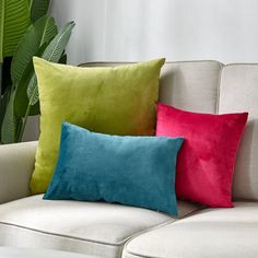 three different colored pillows on a white couch