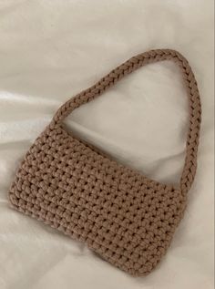 a crocheted purse sitting on top of a white bed next to a pillow