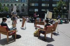 people are sitting in chairs and reading books on the side walk near a city street