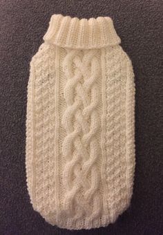 a white knitted dog sweater with a knot on the front and bottom, sitting on a carpet