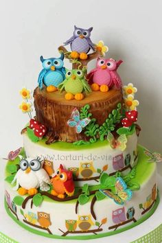 a three tiered cake decorated with colorful owls and flowers on it's side