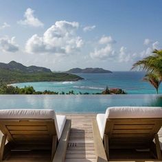 two lounge chairs sitting on top of a wooden deck next to an ocean and mountains