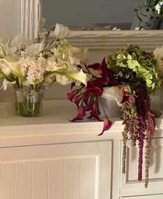 three vases filled with flowers sitting on top of a white dresser next to a mirror