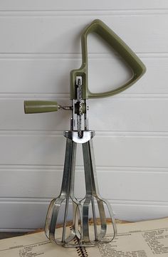 a green kitchen utensil sitting on top of an old recipe book next to a white wall