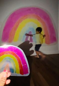 a person holding up a sticker in front of a rainbow painting on the wall