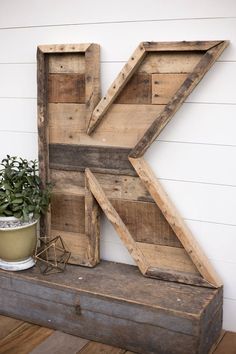 the letter k is made out of wood and sits on a shelf next to a potted plant