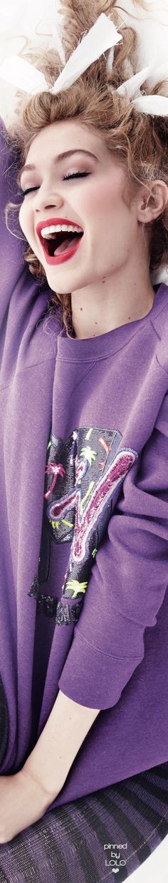 a woman laying on top of a bed wearing a purple shirt