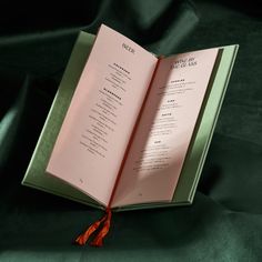 an open book sitting on top of a green cloth covered tablecloth next to a red tassel