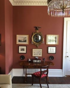 a living room with red walls and pictures on the wall, including a desk in front of a chandelier