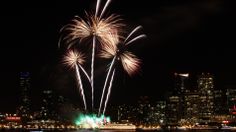 fireworks are lit up in the night sky over water and city buildings as seen from across the bay