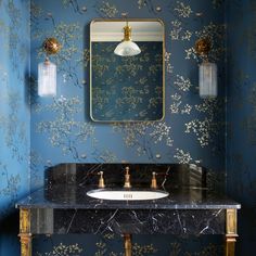 a bathroom with blue and gold wallpaper, marble counter top and vanity sink under a large mirror