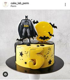 a batman themed birthday cake with stars and bats on the top, sitting on a pedestal