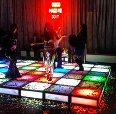 three people standing on a dance floor with colored lights