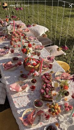 a long table with plates and cups on it in the middle of a field filled with flowers