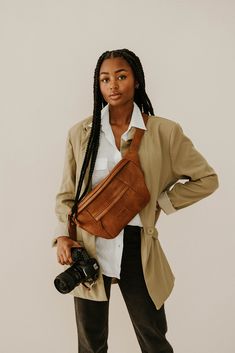 a woman holding a camera in her right hand and wearing a brown leather fanny bag