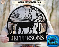 a man holding up a metal sign that says jeffersons with a horse and mountains in the background