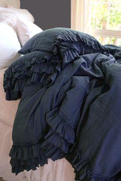 an unmade bed with blue ruffles and pillows on it, in front of a window