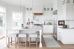 a white kitchen with an island and stools in the center, surrounded by windows