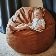 a little boy sitting on a bean bag chair reading a book in his living room