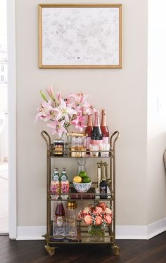 a bar cart filled with bottles and flowers on top of a hard wood floor next to a wall