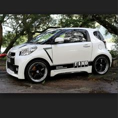 a white smart car parked in front of some trees