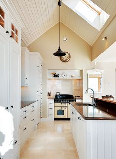 a kitchen with white cabinets and black counter tops, an oven on the wall and a skylight hanging from the ceiling