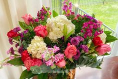 a vase filled with lots of colorful flowers on top of a wooden table next to a window