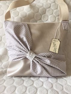 a gray and white polka dot purse with a tag on the front, sitting on a bed