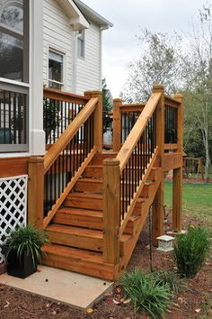 a wooden deck with railing and planters next to the front door, on a sunny day