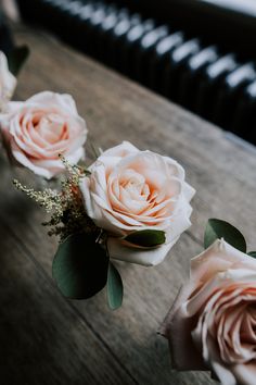 three pink roses sitting on top of a wooden table next to a black piano keyboard