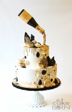 a three tiered cake decorated with black and gold decorations, champagne being poured on top