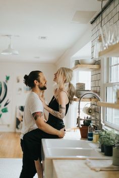 a man and woman standing in front of a kitchen sink looking at each other's eyes