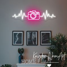 the neon sign above the fireplace has three pictures on it and is next to a potted plant