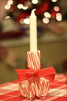 a white candle sitting on top of a table next to a red and white checkered table cloth