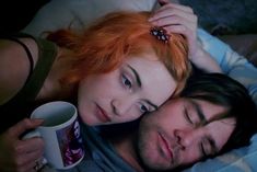 a man and woman laying next to each other on top of a bed holding coffee mugs