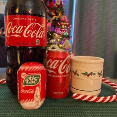 coca - cola cans, cups and candy canes are sitting on a table in front of a christmas tree