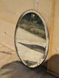 a round mirror sitting on the side of a wall next to a cement block and grass