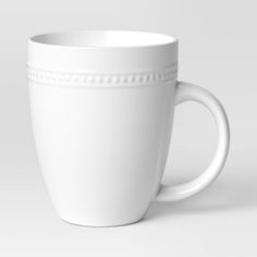 a white coffee cup with beaded trim around the rim and sides on a plain background